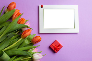 Empty picture frame next to a bouquet of tulips and a red gift box