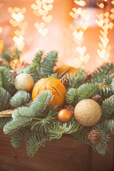Fototapeta na wymiar Christmas mood. Beautiful festive arrangement of fresh spruce in a rustic wooden box. Bokeh hearts of Garland lights on background. Decorated with slices orange, gold balls , cones