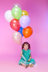 Fototapeta na wymiar Portrait of a cheerful little toddler girl over pink background, holding bunch of colorful air balloons. The concept of children holiday birthday