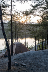 Tent in the woods on the shore of a quarry with blue water at dusk in summer Travel as a lifestyle...