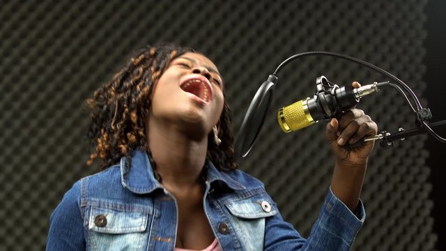 African american alfro hair black Woman sing a song loudly and express feeling with power sound over hanging microphone condenser. Egg Crate Studio low lighting shadow Sound Proof Absorbing wall room