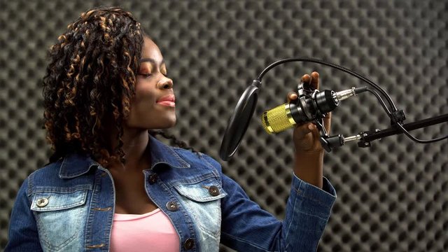 African american alfro hair black Woman sing a song loudly and express feeling with power sound over hanging microphone condenser. Egg Crate Studio low lighting shadow Sound Proof Absorbing wall room