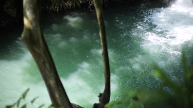 Slow Motion shot of a man doing a back-flip into the swimming hole at Aling-Aling Waterfall in Bali, Indonesia.