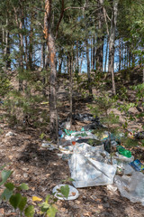Obraz premium Plastic, paper and other rubbish is scattered among the trees in the forest on a summer day. Environmental pollution by waste after outdoor recreation. Vertical