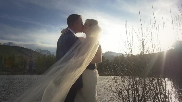 Bride with a long veil kisses the groom at their mountain wedding