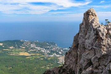 view of the resort city of Yalta from the top of Mount Ai-Petri, on a bright sunny day with clouds in the sky.