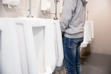 A man peeing to the toilet bowl in the restroom