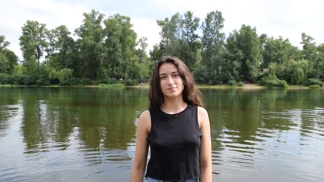 Portrait of a young brunette girl near the water on a green forest background.