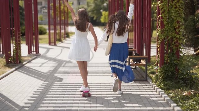 Young girl helps her friend as she learns to ride a skateboard