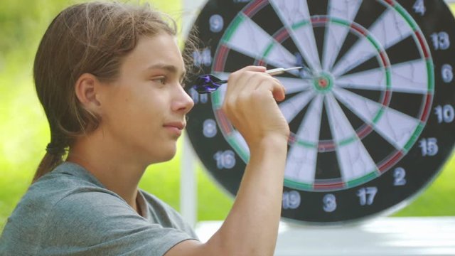 Portrait of a teenager boy playing darts. A boy plays an outdoor darts game.