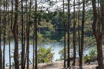View of a quarry filled with clear blue water through the trees on a summer sunny day. Tourism and travel as a lifestyle