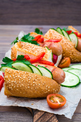 Ready-to-eat hot dogs from fried sausages, sesame buns and fresh vegetables on a cutting board on a wooden table