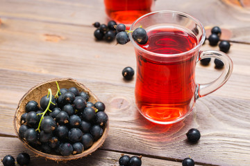 Fresh ripe black currant compote in a glass and a bowl of berries on a wooden table