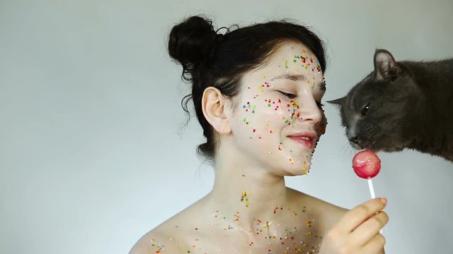 Beauty girl with baby face treating the cat with candy. Portrait of a young pretty girl