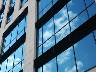 angled view of a modern commercial building with large mirrored windows reflecting blue sky and white clouds