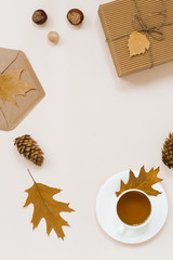 Autumnal flat lay with white knitted plaid, hot Cup of tea and fallen brown leaves, crab envelope, gift box. Top still life autumn concept on beige light background with copy space.