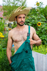 handsome gardener with green pants and straw hat standing in garden