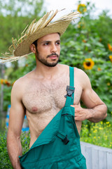 handsome gardener with green pants and straw hat standing in garden