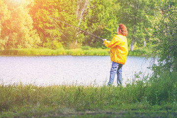 Fototapeta na wymiar Woman in yellow jacket fishing spinning on the lake in sunlight