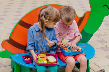 Girl and boy preschool students eating their lunches from lunch boxes