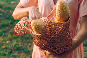 Young woman holding mesh bag with baguettes outdoors