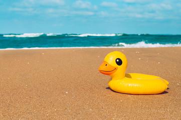 Inflatable rubber duck swimming ring on the sand near sea on the beach