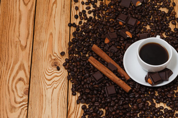 Cup of coffee in a white cup and coffee beans, chocolade, cinamon sticks on wooden background