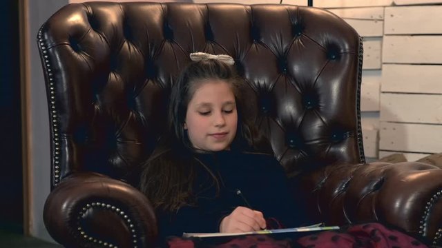Small pretty girl painting a picture sitting in a leather armchair and then showing it to her parent who is pround of her talent