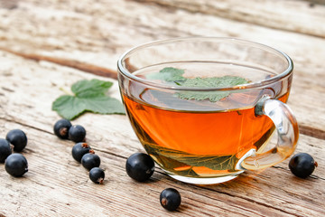 Currant leaf herbal tea in a glass transparent cup on a wooden table near the leaves and berries of green currant.