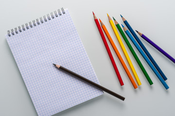 Clean notepad in a cage with a pencil lying on it and rainbow color pencils on a white background top view copy space