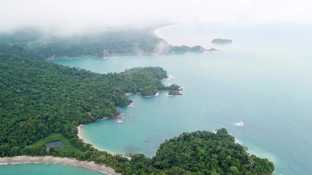 Aerial, pan, drone shot, overlooking beaches, turquoise waters and rainforest, on the coast of Herradura bay, on a foggy and cloudy, summer day, in Jaco, Costa Rica