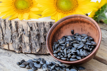 Yellow sunflowers and sunflower seeds in a bowl on a wooden background.