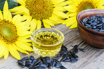 Obraz na płótnie Canvas Sunflower oil and sunflower seeds in a bowl on a wooden background near fresh sunflower flowers. Organic and eco food.