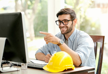 Handsome engineer man with smiling point his finger to computer monitor and sit in the office with...