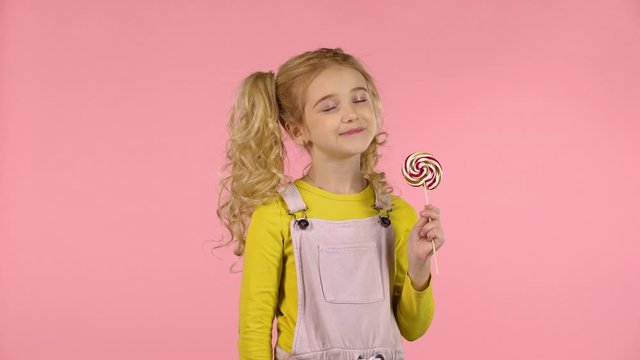 Beautiful girl with a lollipop in studio on pink background