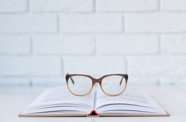 open book and glasses for vision on a table on a background of a white brick wall with a place for text. back to school, horizontal frame