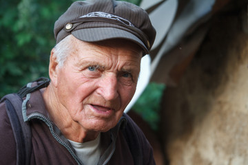 Close-up portrait of a very old man in a cap on a blurred background of green trees, selective focus