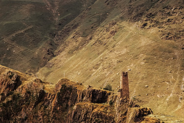 Ancient fortress tower and a white cross stand on the bluffs of the Caucasus Mountains in Georgia...