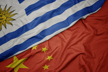 waving colorful flag of china and national flag of uruguay.