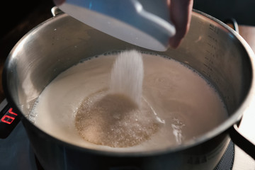 pouring sugar into milk into a pan on scales.