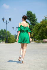 Young beautiful brunette girl in green dress walks along the embankment of the river Volga in Samara