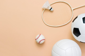Assorted sports equipment including a basketball, soccer ball, volleyball, baseball, badminton racket on a light brown background