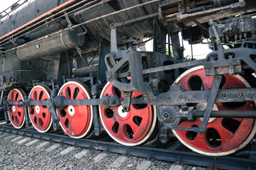Red wheels of an old black locomotive on the rails close-up.