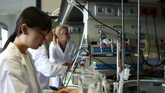 Intelligent Chinese girl working with reagent in test tube during chemical experiment with  fellow students in university lab 