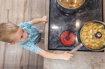 Little boy playing with pan on electric stove in the kitchen. Top view. Safety child