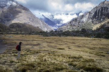 Naklejka premium Trail to Laguna 69. A person standing looking at the beautiful landscape of the mountains. There are small bushes around it and huge mountains behind with snowy peaks and clouds. Peru