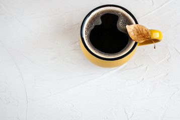 Bright yellow cup with a hot coffee drink, on a cup a dry autumn orange leaf on a white background.