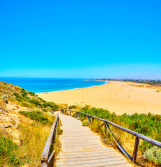 Fototapeta na wymiar Wooden boardwalk going to Faro de Trafalgar Beach, a broad beach of The Cabo de Trafalgar Cape Natural Park. Barbate, Los Caños de Meca, Cadiz. Andalusia, Spain.