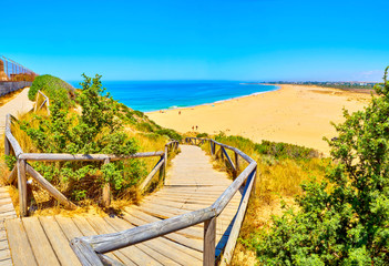 Obraz premium Wooden boardwalk going to Faro de Trafalgar Beach, a broad beach of The Cabo de Trafalgar Cape Natural Park. Barbate, Los Caños de Meca, Cadiz. Andalusia, Spain.