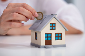 Woman Inserting Coin In House Piggybank